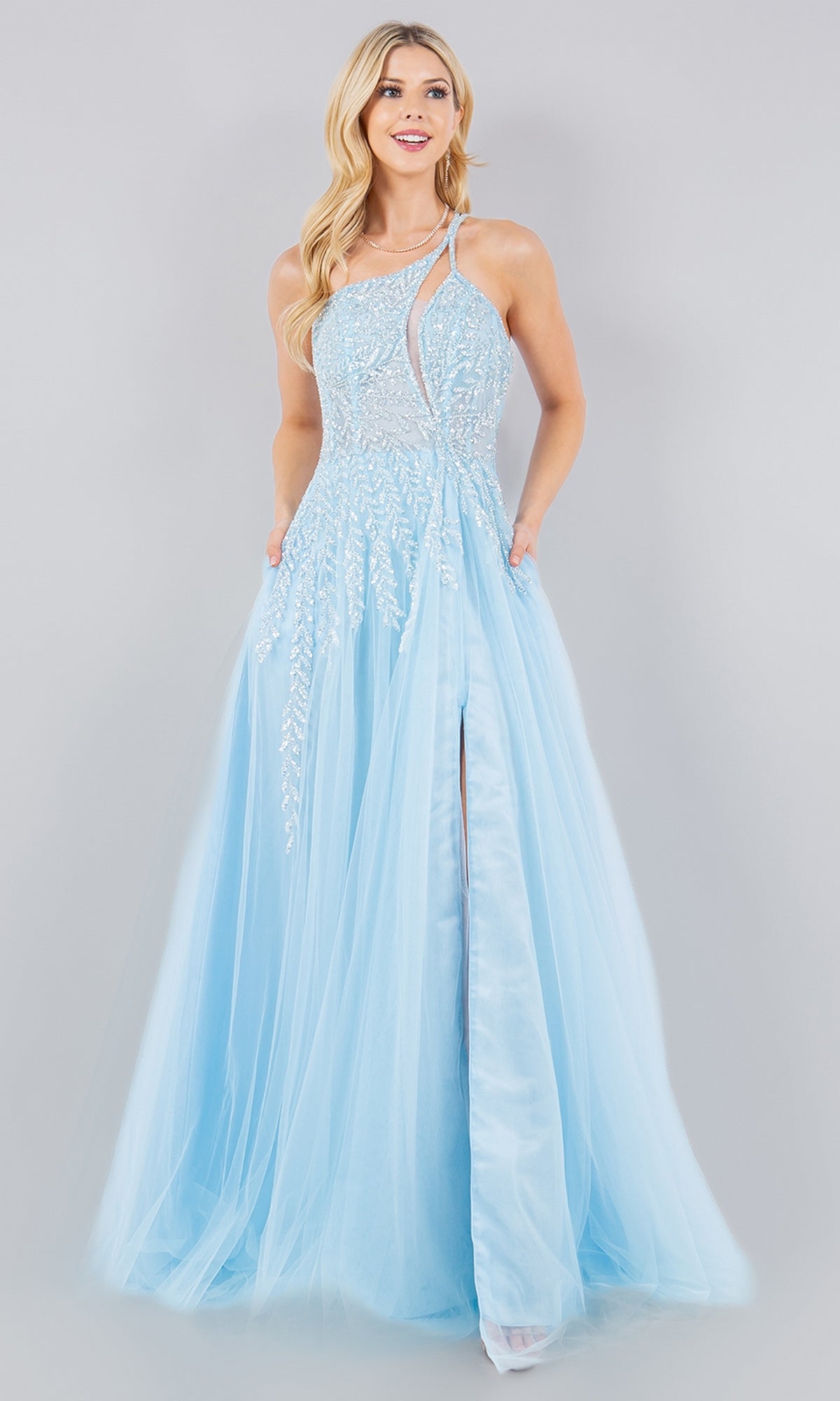 A woman wears the Pastel Tulle Prom Dress: Cinderella Couture 8118J, a light blue, floor-length gown with a sheer overlay, intricate embroidery, high slit, asymmetrical neckline, and delicate sequin vine print for elegance.